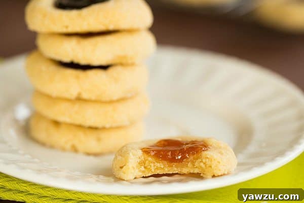 A close-up of the perfectly baked Classic Thumbprint Cookies, showcasing their golden edges and luscious jam filling. The ultimate Christmas cookie recipe.