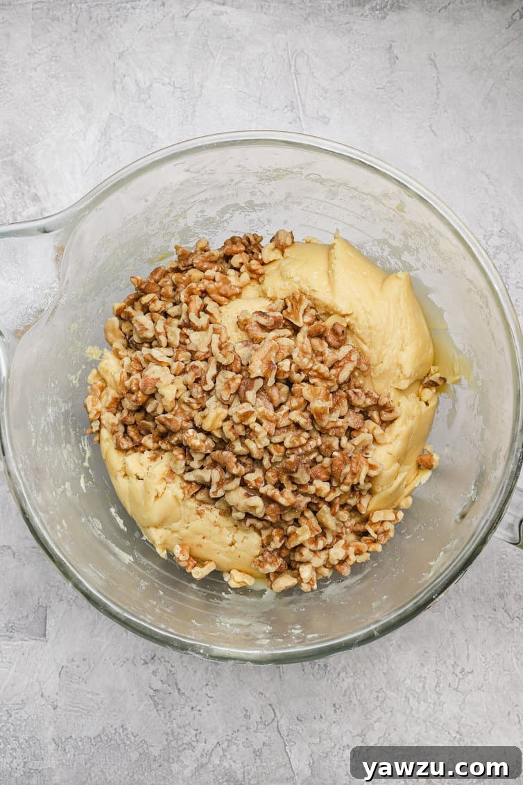 Biscotti dough in a clear glass bowl, generously mixed with chopped walnuts, ready for shaping.