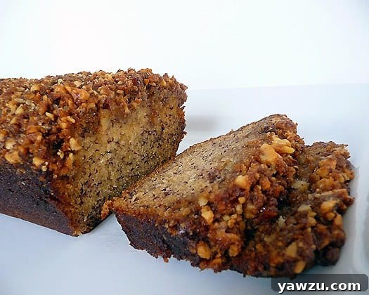 Two slices of Bananas Foster Banana Bread displayed next to the full loaf on a white plate, highlighting the delicious streusel topping and moist interior.