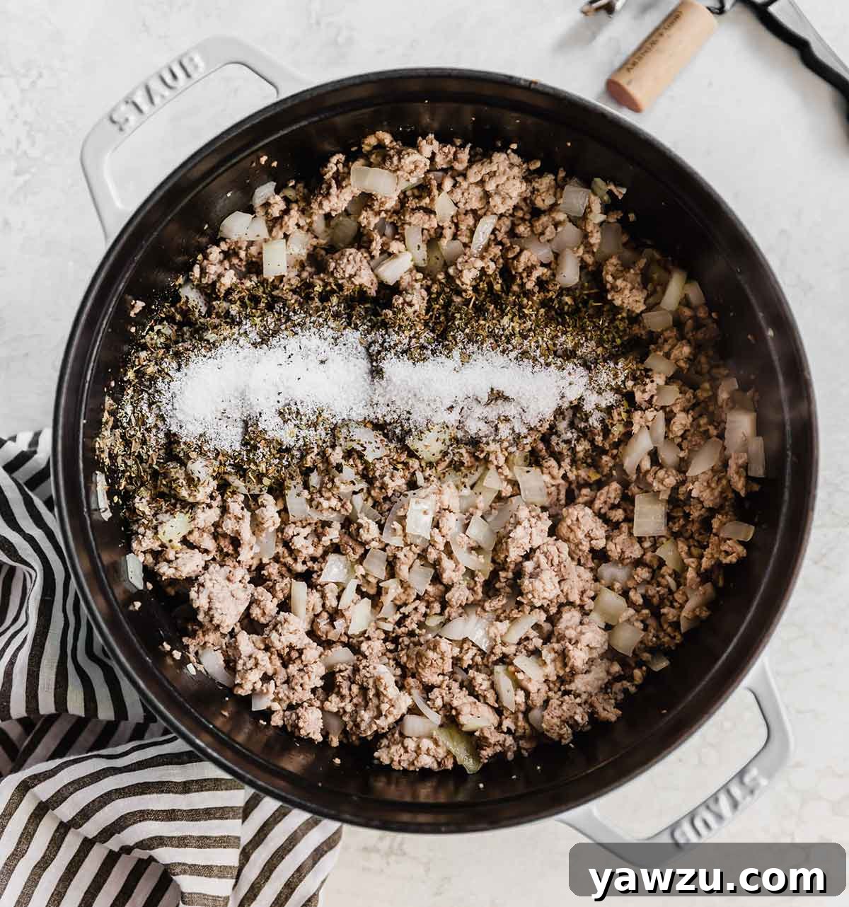 Overhead photo of a pot with browned meat, onions, garlic, and seasonings.