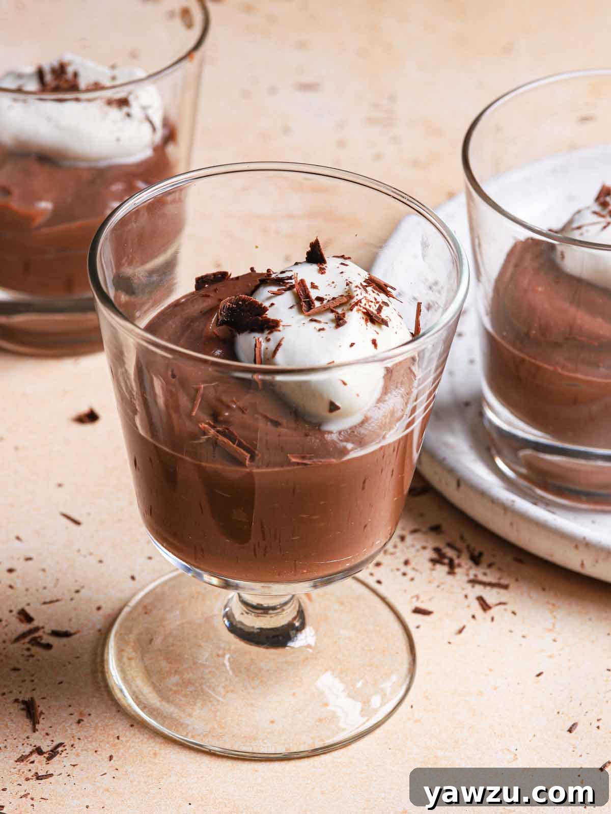 Small glass cups filled chocolate pudding and topped with whipped cream and chocolate shavings.