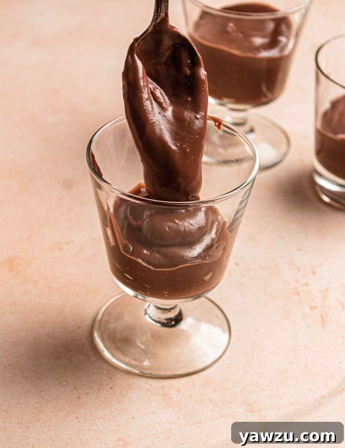 Chocolate pudding being spooned into glass parfait cups.