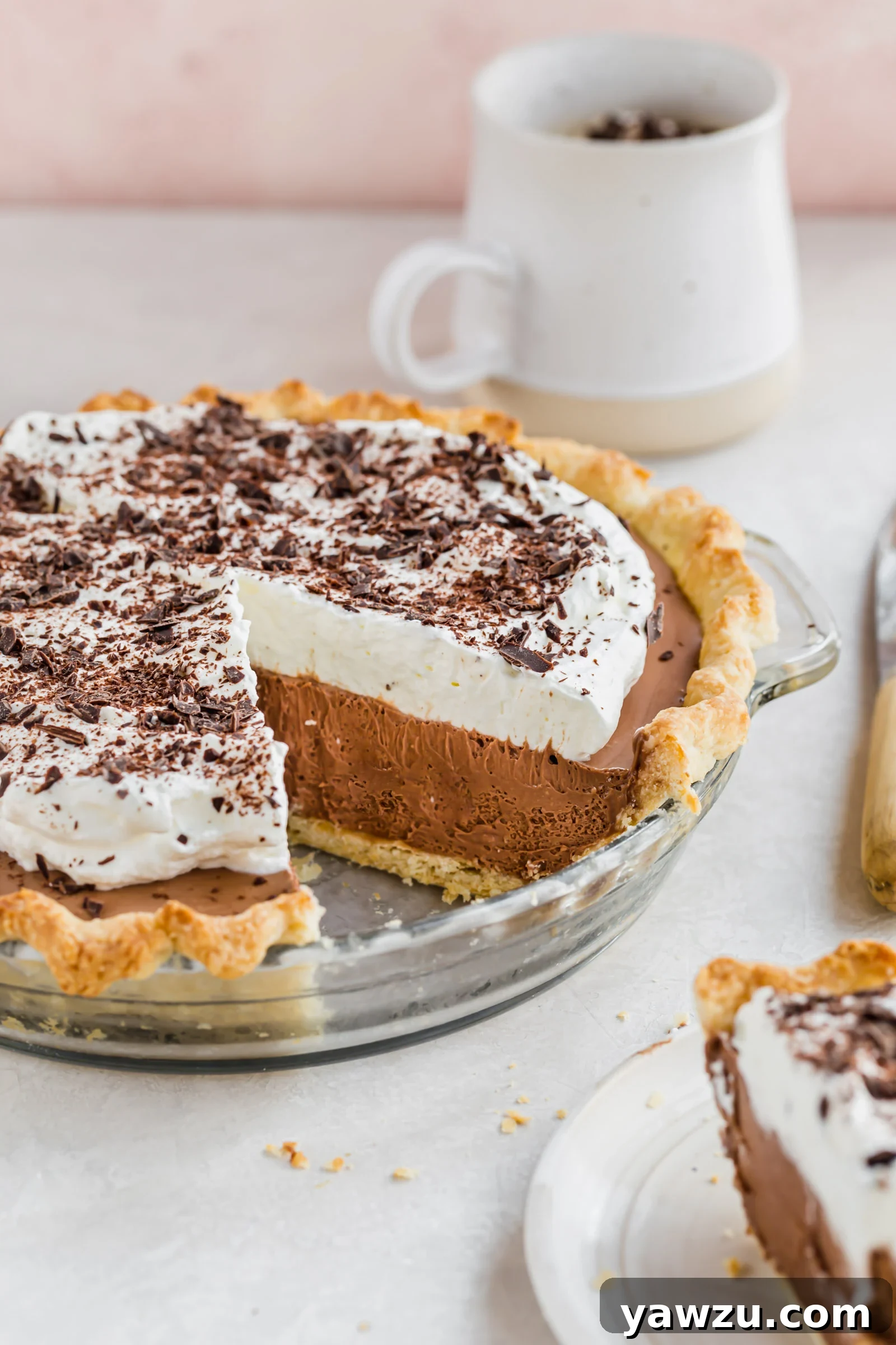 Side view of French silk pie in glass pie plate with one slice removed and coffee mug in background.