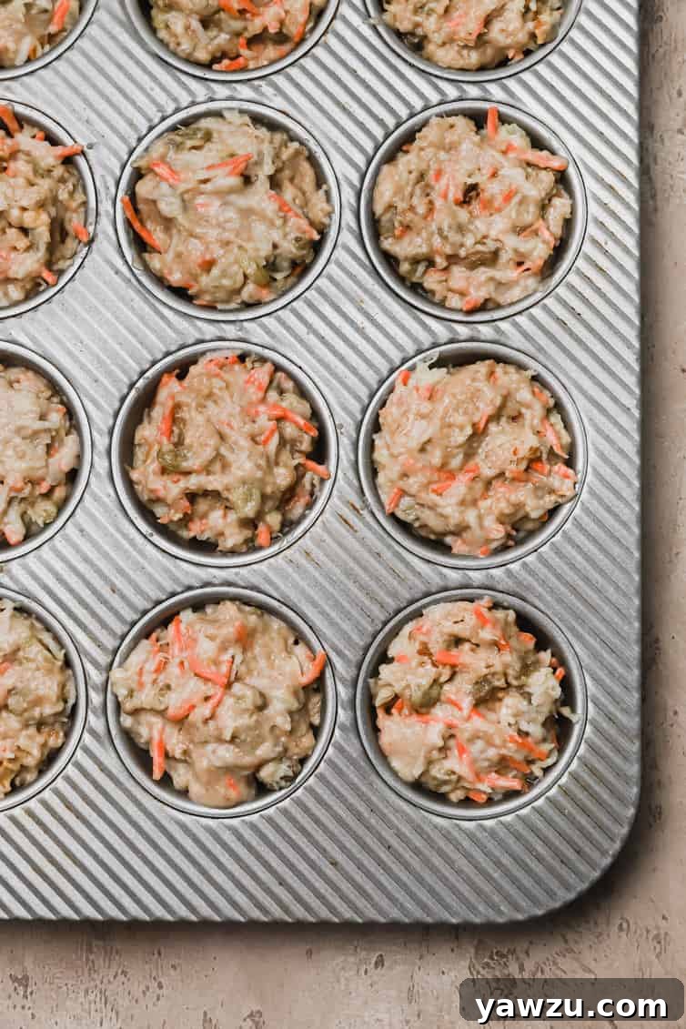 Morning Glory Muffin batter meticulously divided into a muffin pan, showcasing the rich texture and visible inclusions before baking to golden perfection.