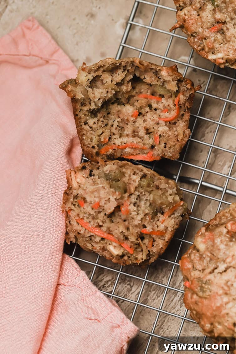 A perfectly baked Morning Glory Muffin, cut in half to reveal its moist, fruit and nut-filled interior, sitting invitingly on a wire cooling rack.
