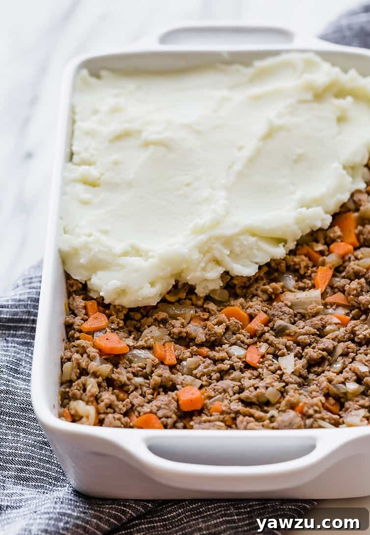 The savory meat mixture for Shepherd's Pie fills a casserole dish, with creamy mashed potatoes being carefully spread on top to create an even layer.