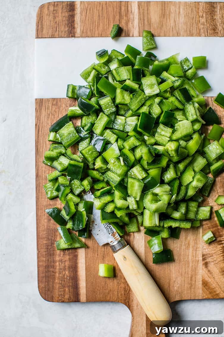 Chopped jalapeno and poblano peppers on a wooden cutting board.