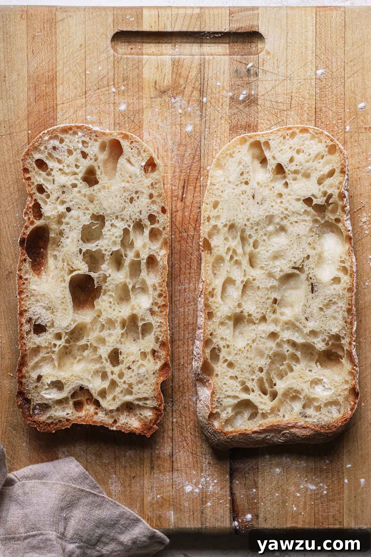 A loaf of baked ciabatta bread sliced in half horizontally and both halves laid out cut-side-up on a cutting board, ready for sandwiches or dipping.