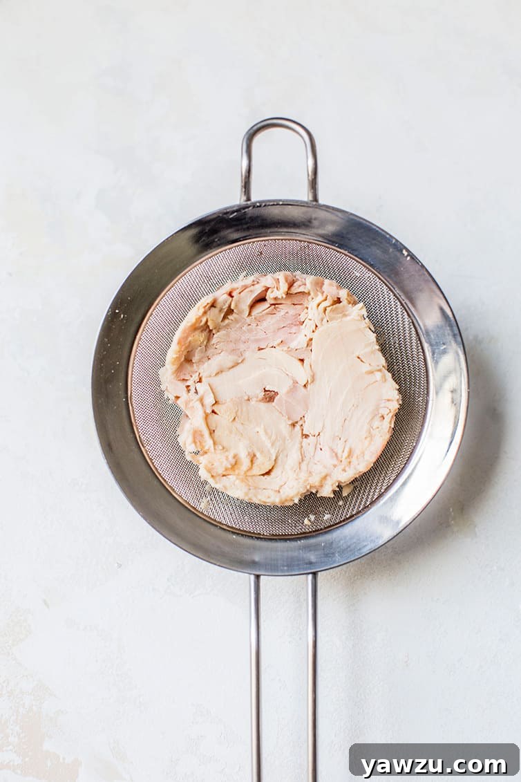 Flaked tuna being drained in a fine mesh sieve to ensure excess water is removed, crucial for a perfectly moist casserole.