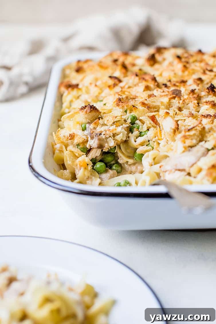 A close-up, head-on view of a pan of golden-brown tuna noodle casserole, with a generous portion scooped out, showcasing its rich texture.
