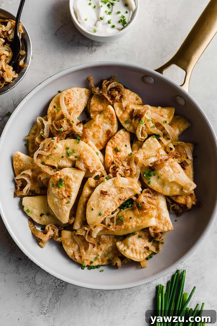A frying pan full of golden-brown homemade pierogi with caramelized onions, ready to be served.