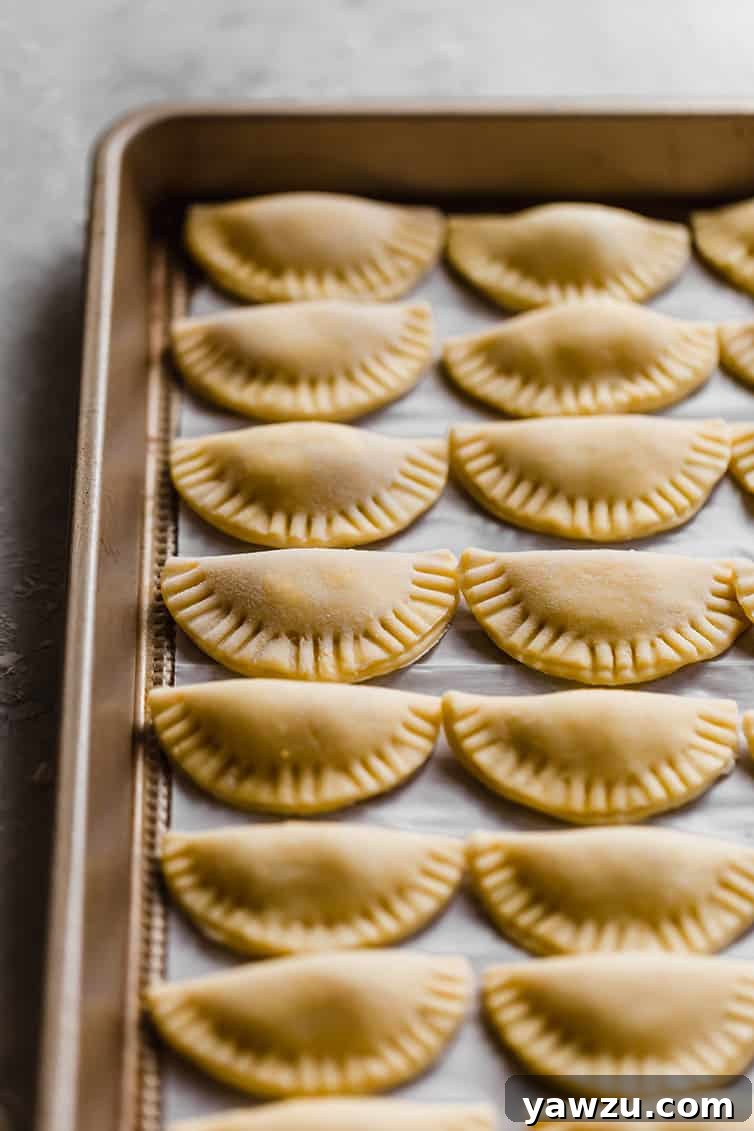 A baking pan filled with rows of assembled, uncooked pierogi, ready for boiling or freezing.