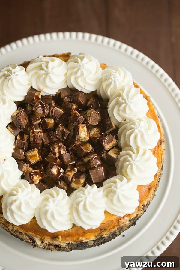 Indulgent Snickers Cheesecake, topped with whipped cream, chopped Snickers, hot fudge, and caramel sauce.