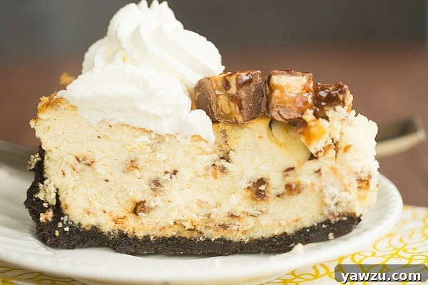 Snickers Cheesecake slice with generous topping of chopped Snickers, caramel, and fudge.