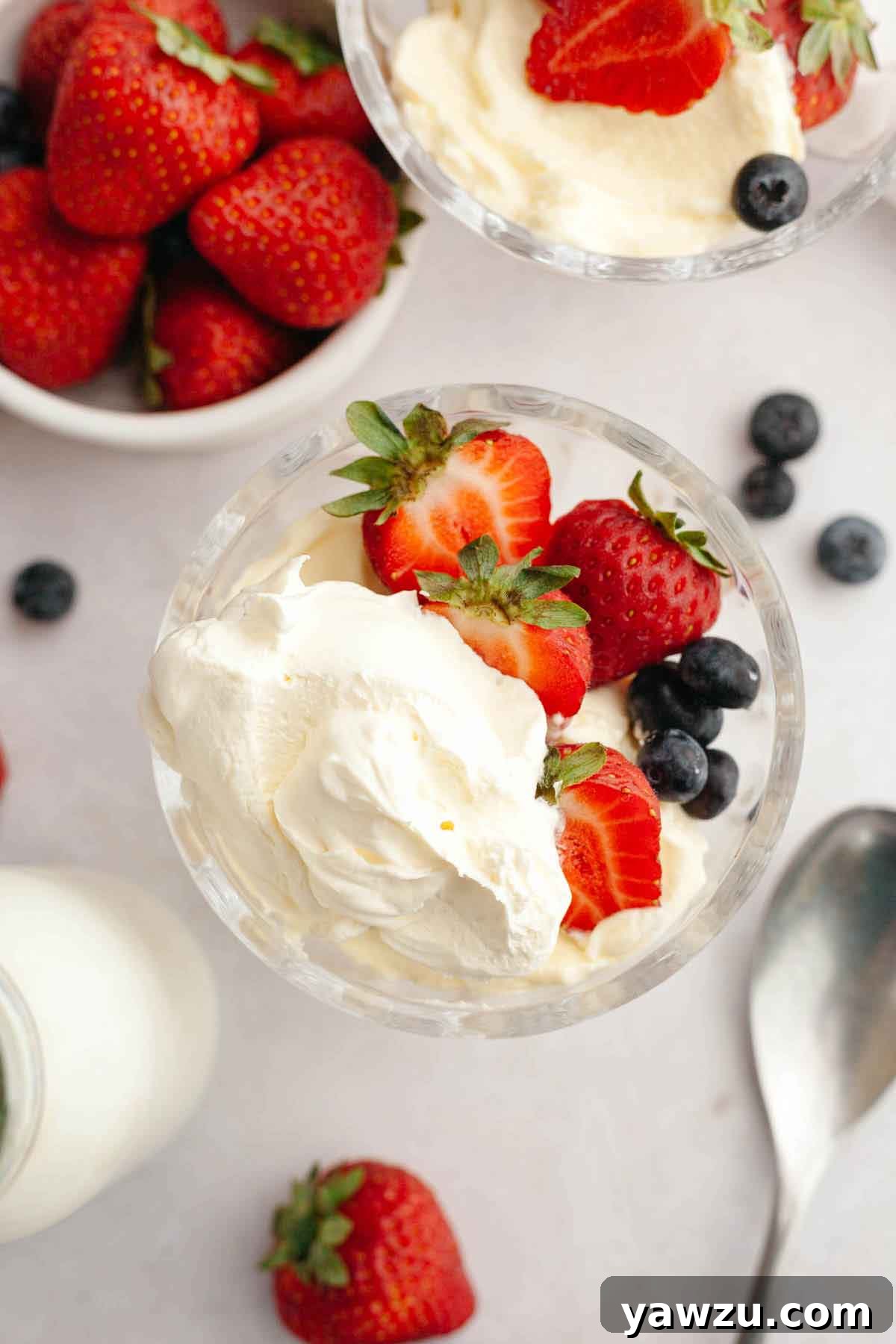 Overhead photo of a glass bowl with strawberries, blueberries, and fresh whipped cream.