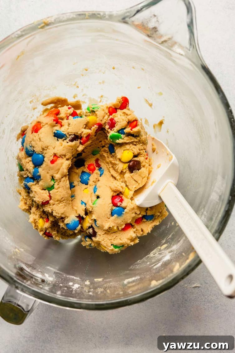 M&M cookie dough in a clear glass mixing bowl, showing the colorful candies mixed in.