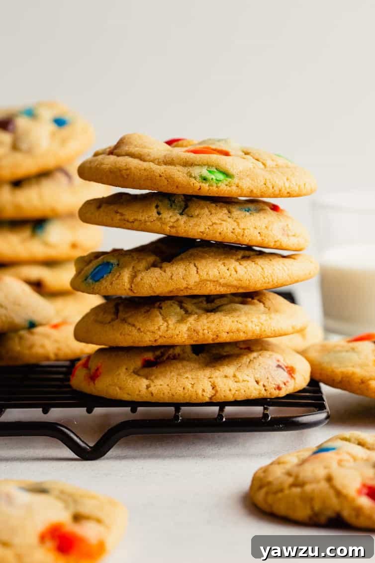 A stack of golden-brown M&M cookies cooling on a wire rack.