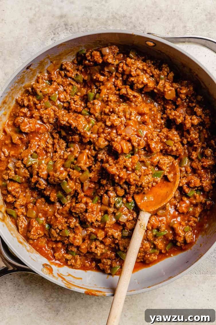 Homemade sloppy joe meat in a skillet with a wooden spoon.