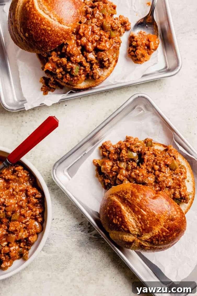 Two metal trays lined with parchment paper with homemade sloppy joes on top of the parchment paper with a small skillet of sloppy joe meat to the left.
