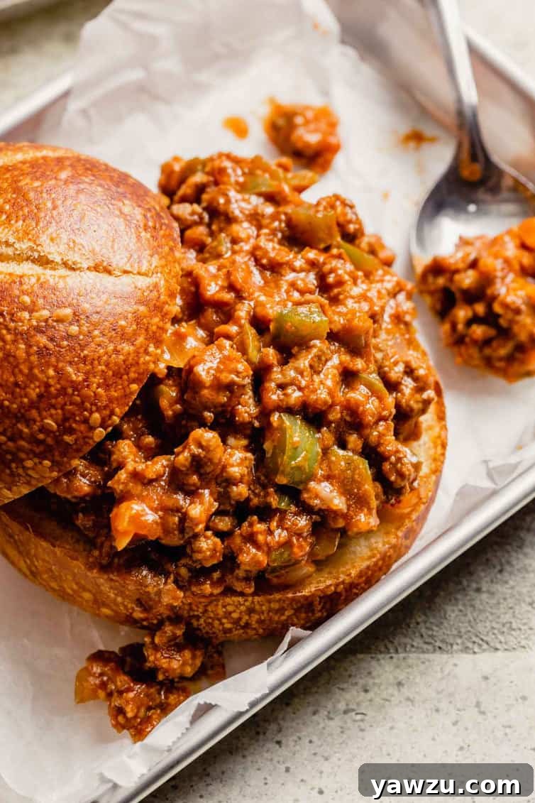 Homemade sloppy joes with the bun top pulled back and a spoon of sloppy joe meat to the right.