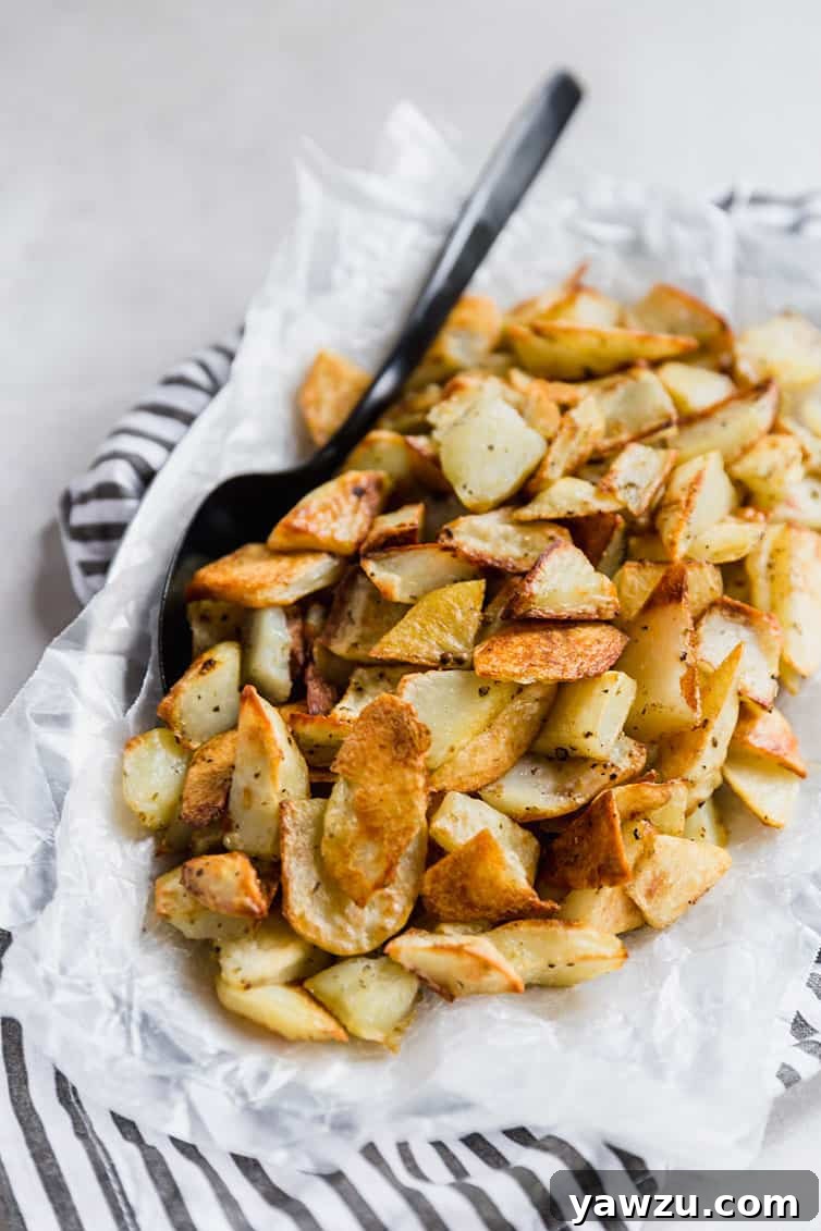 A rustic bowl filled with golden crispy roasted potatoes, ready to be served, with a serving spoon nestled within.