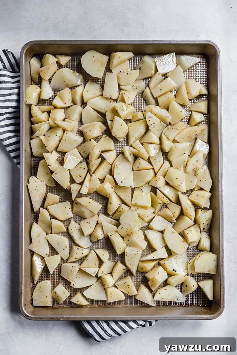 A baking pan filled with freshly sliced russet potatoes, generously tossed with olive oil and Italian seasoning, ready for roasting.