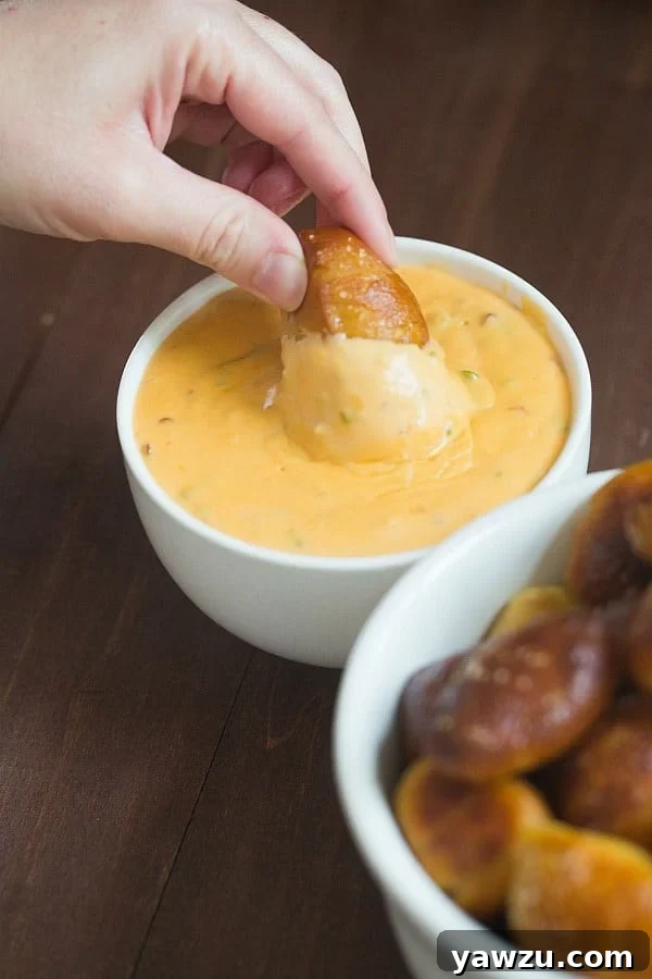 Close-up of a soft pretzel nugget being dipped into the vibrant, creamy spicy cheese sauce.