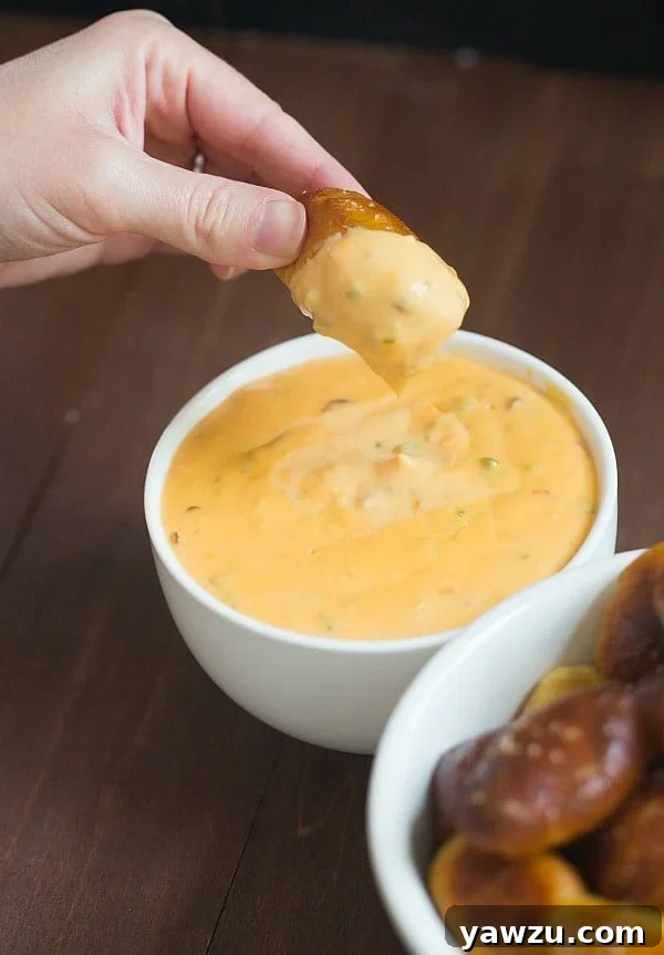A bowl of spicy cheese dipping sauce with pretzel nuggets in the background, ready to be served.