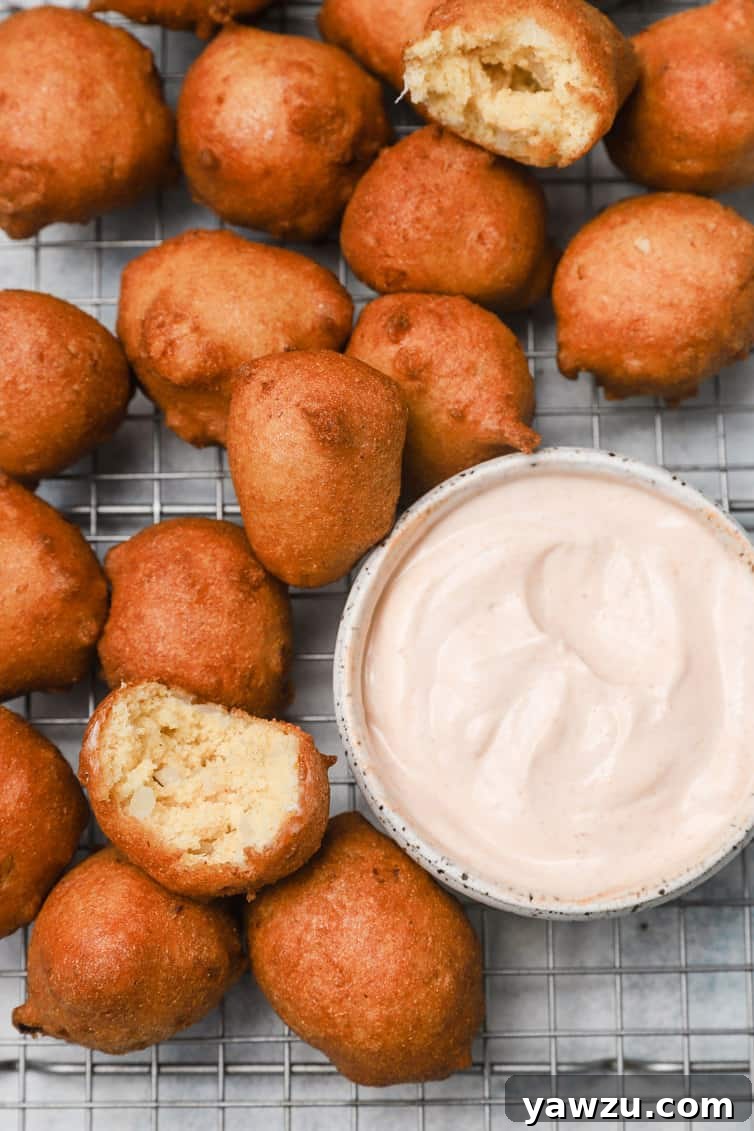 Crispy hush puppies arranged on a wire rack, accompanied by a small bowl of spicy dipping sauce.