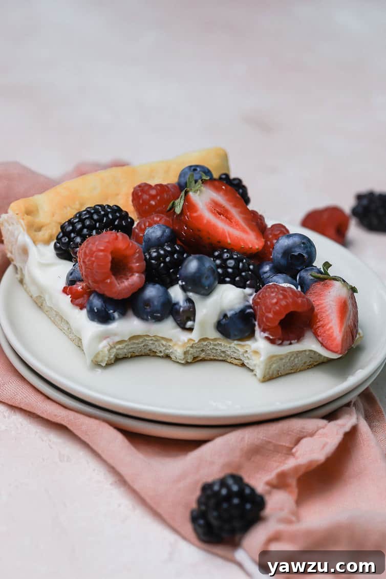 A slice of fruit pizza on a plate with two bites taken out.