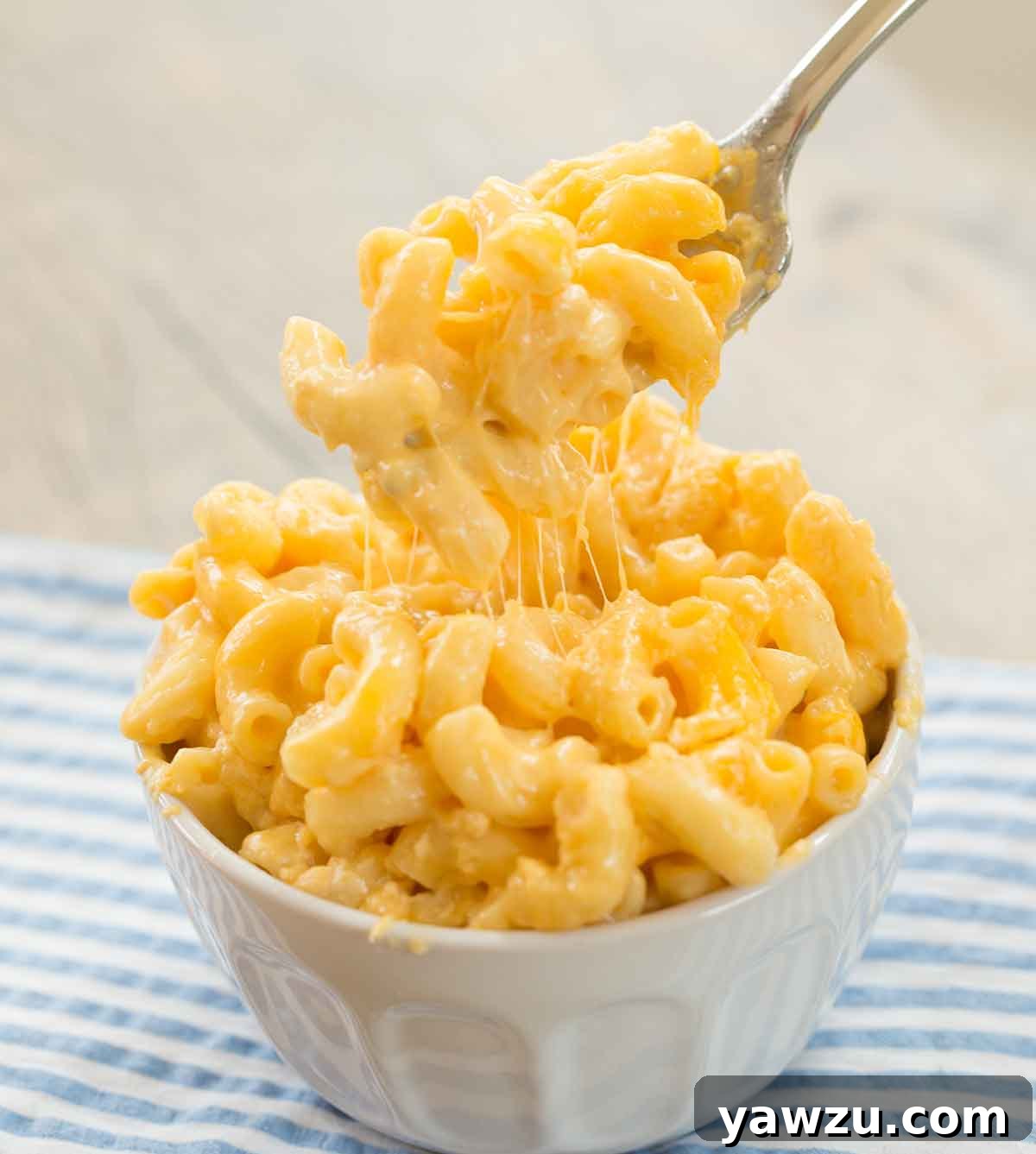 A fork scooping up cheesy mac and cheese from a small white bowl.