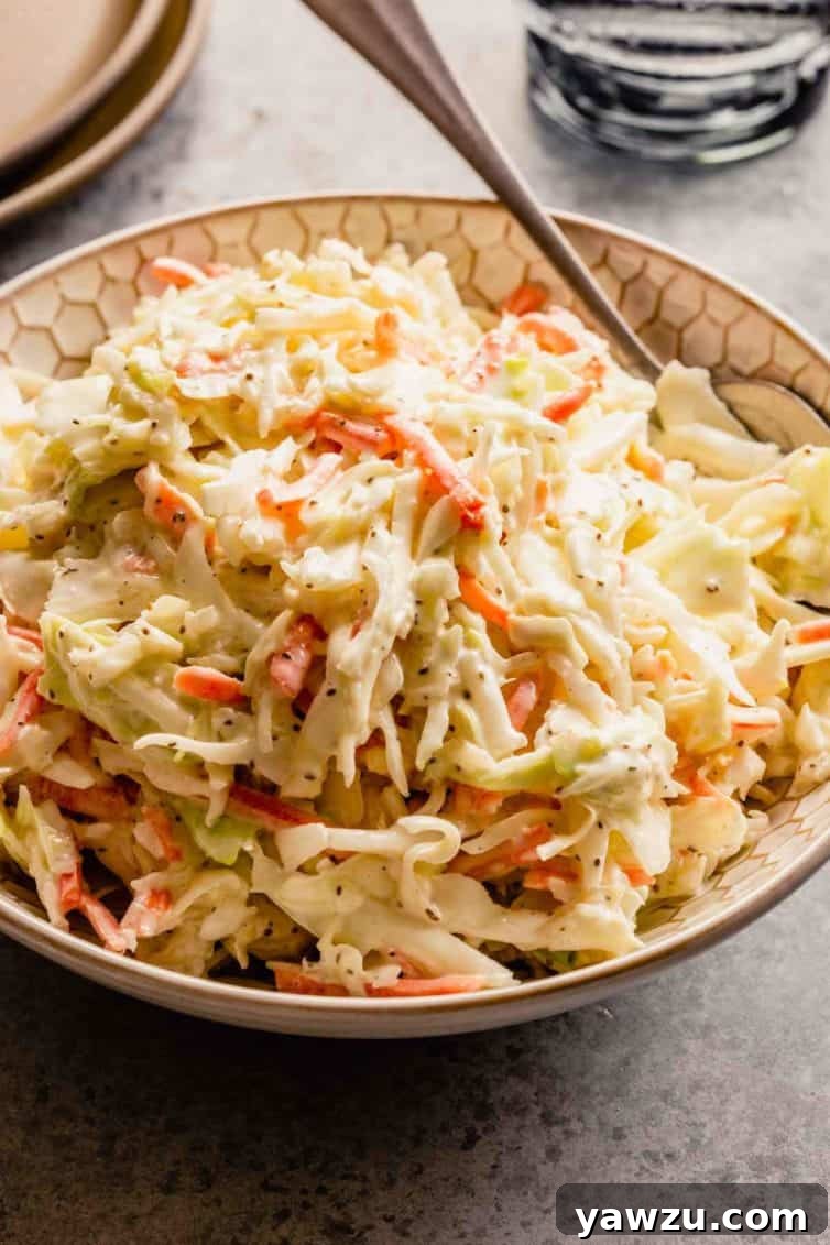 A bowl of creamy coleslaw with a silver spoon on a grey counter.