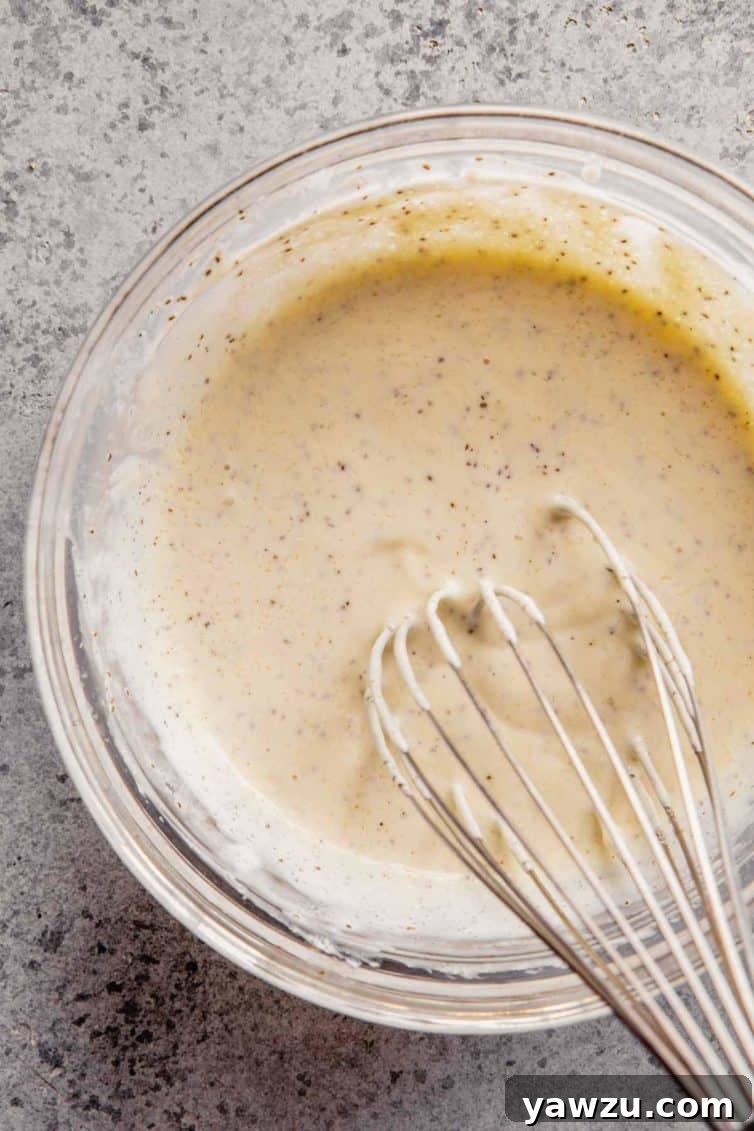 Glass bowl on the counter with a whisk with the coleslaw dressing after mixing.