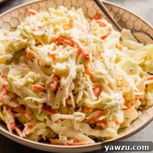 A white bowl with creamy homemade coleslaw and a silver spoon on the right side of the bowl.