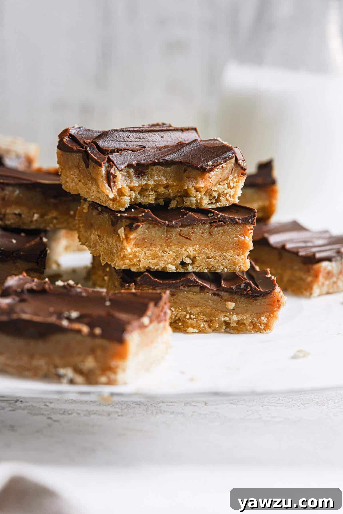 A stack of Millionaire's shortbread bars on a piece of parchment paper with the top bar missing a bite and a jug of milk in the back.