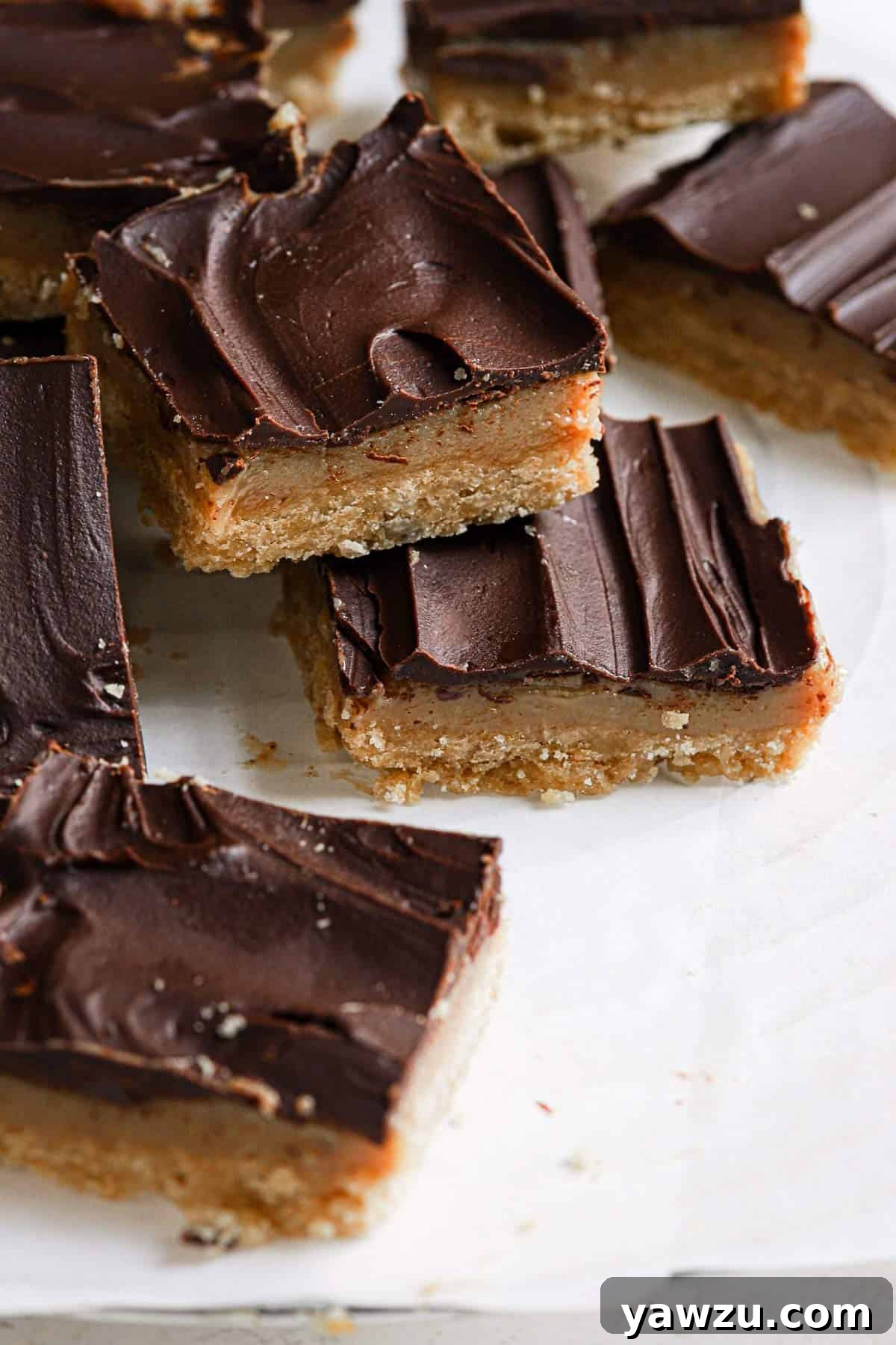 Millionaire bars cut into squares on parchment paper with one stacked on another in the front.