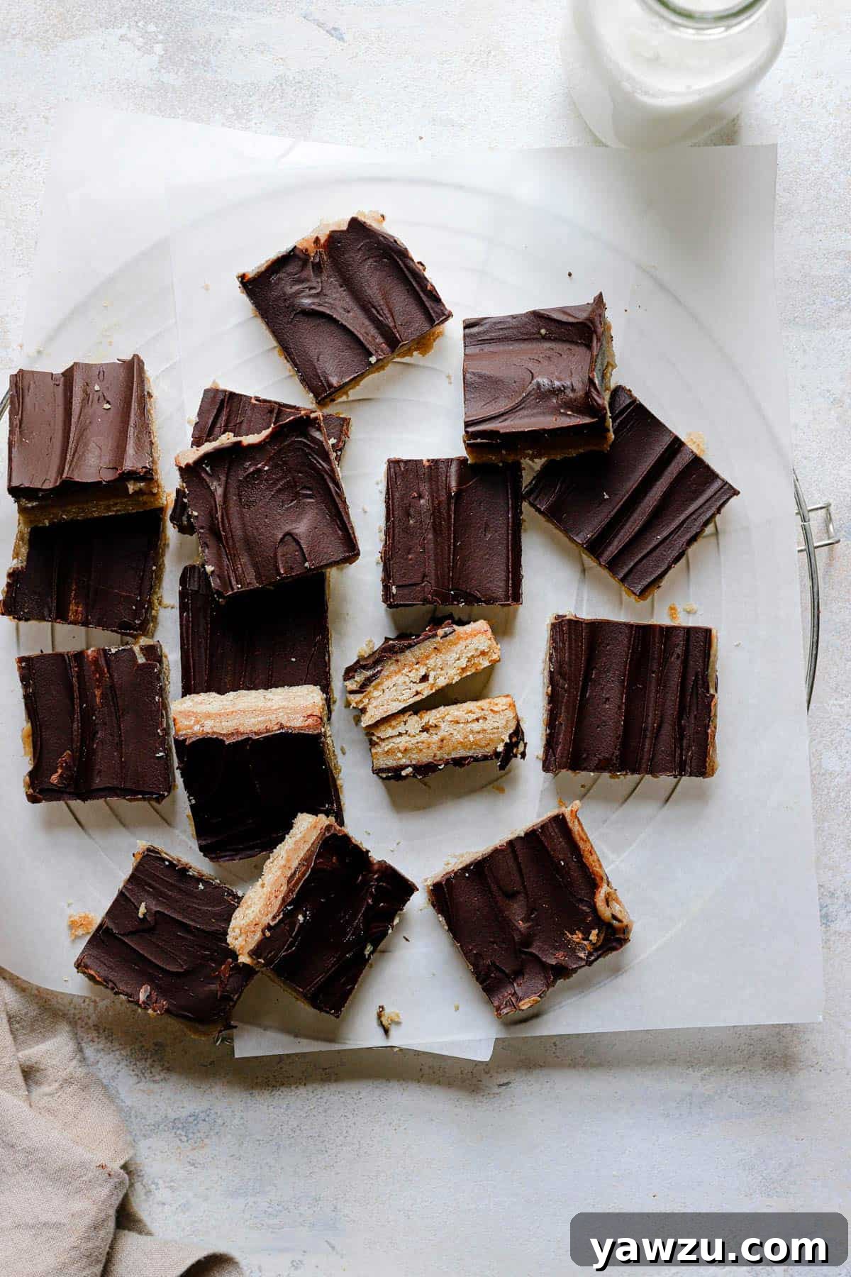 Top down photo of shortbread bars on a cooling rack topped with parchment paper and a glass of milk in the top right corner.