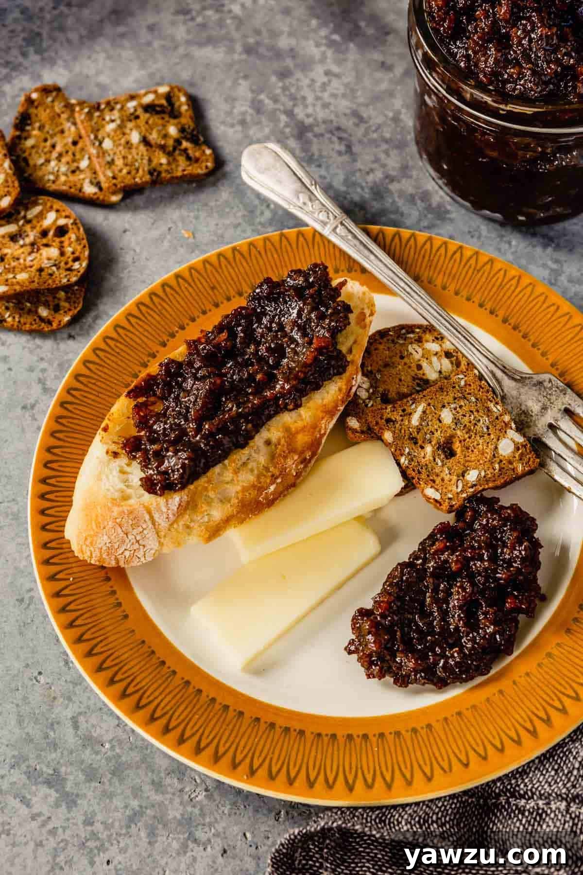 An elegantly arranged plate featuring crusty bread generously topped with homemade bacon jam, alongside artisanal cheese and crisp crackers.