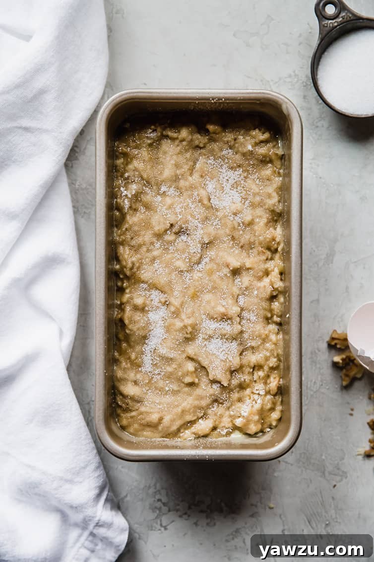 Banana bread batter in a loaf pan with a generous sprinkling of sugar on top, ready for baking.