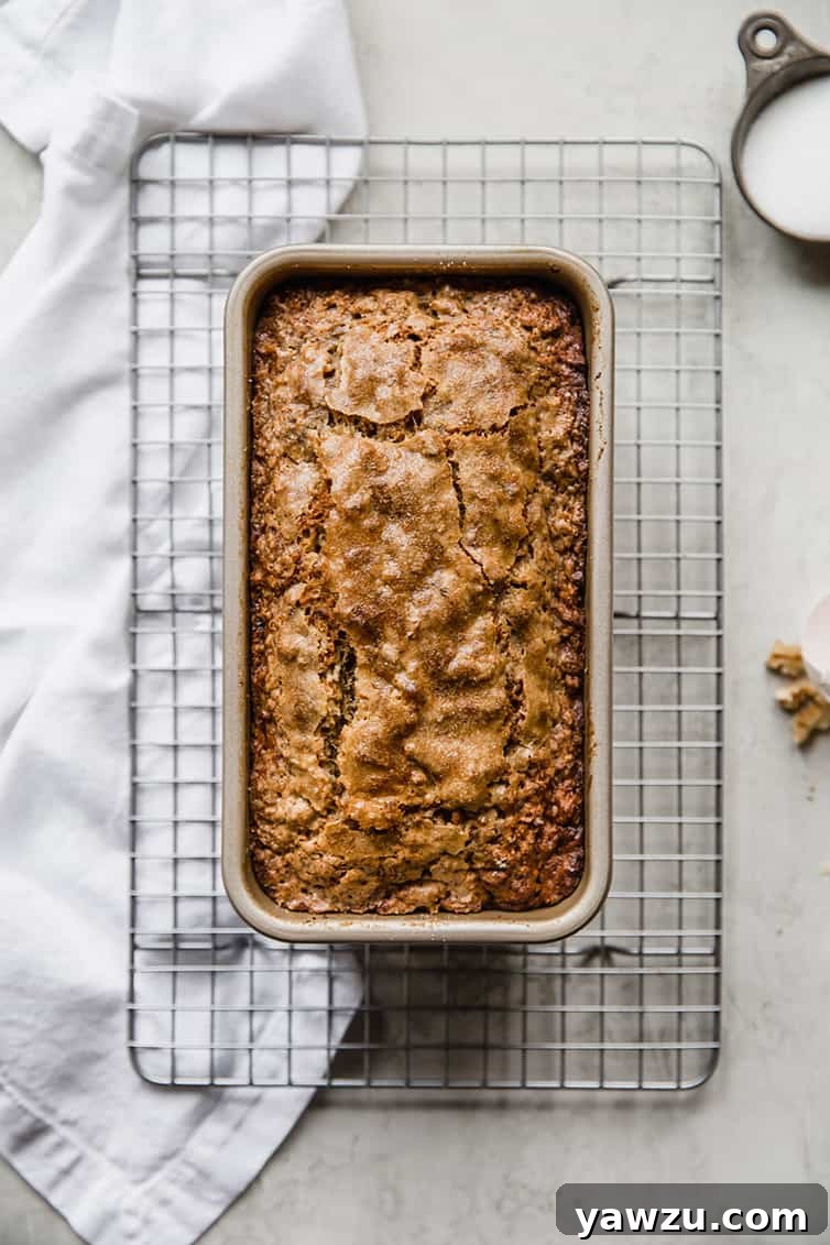 A perfectly baked loaf of banana bread still nestled in its loaf pan on a wire rack.