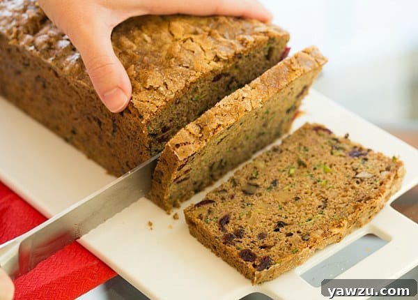 Close-up of a slice of Spiced Zucchini Bread, showing its moist interior, flecks of zucchini, and vibrant dried cranberries and walnuts.