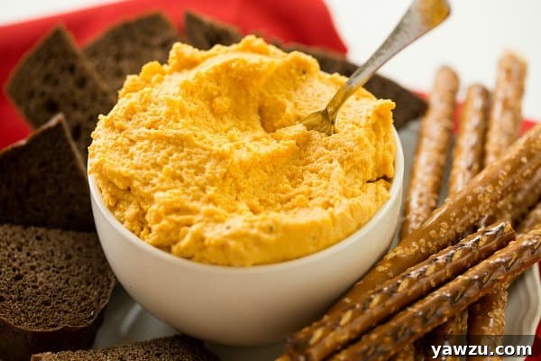 A bowl of Oktoberfest German Beer Cheese Spread garnished with paprika, surrounded by assorted crackers and bread