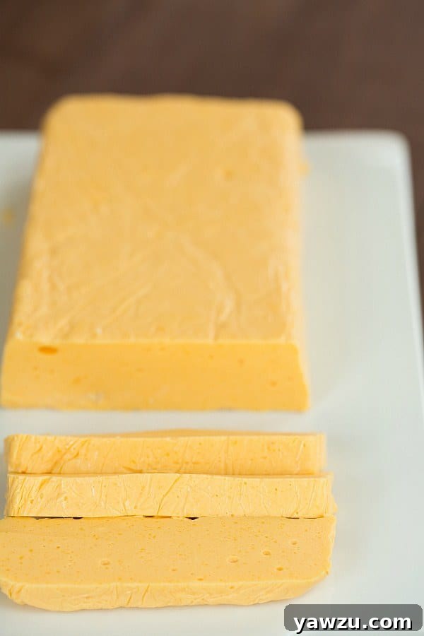 Two blocks of homemade Velveeta cheese, one whole and one sliced, showcasing its smooth texture.