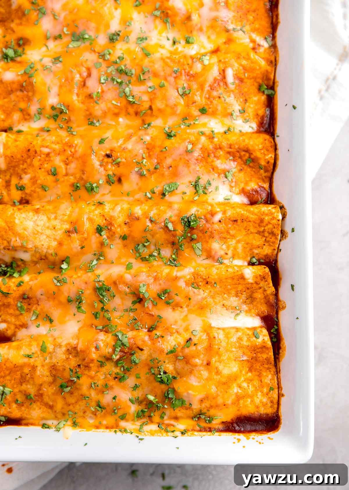 An overhead close-up shot of perfectly baked beef enchiladas still in their casserole dish, showing the bubbly cheese topping and rich red sauce.