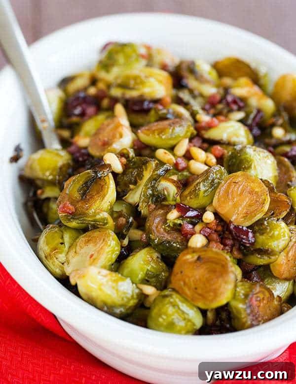 A beautifully plated dish of roasted Brussels sprouts with crispy pancetta, bright red cranberries, and golden pine nuts, perfect for a Thanksgiving feast.