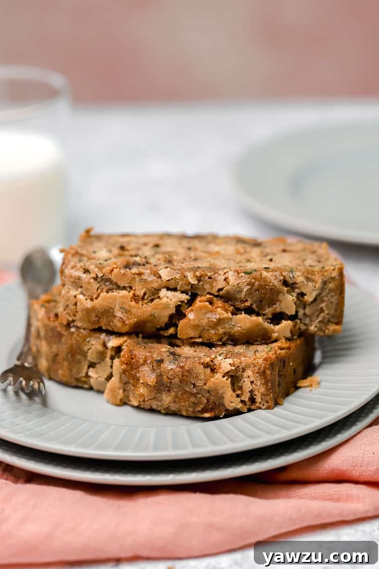 Two perfectly sliced pieces of homemade zucchini bread stacked together on a pristine white plate, highlighting their beautiful crumb and inviting texture.