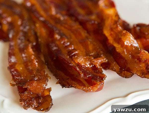 Three slices of Bourbon-Brown Sugar Bacon on a white plate, ready to be enjoyed.