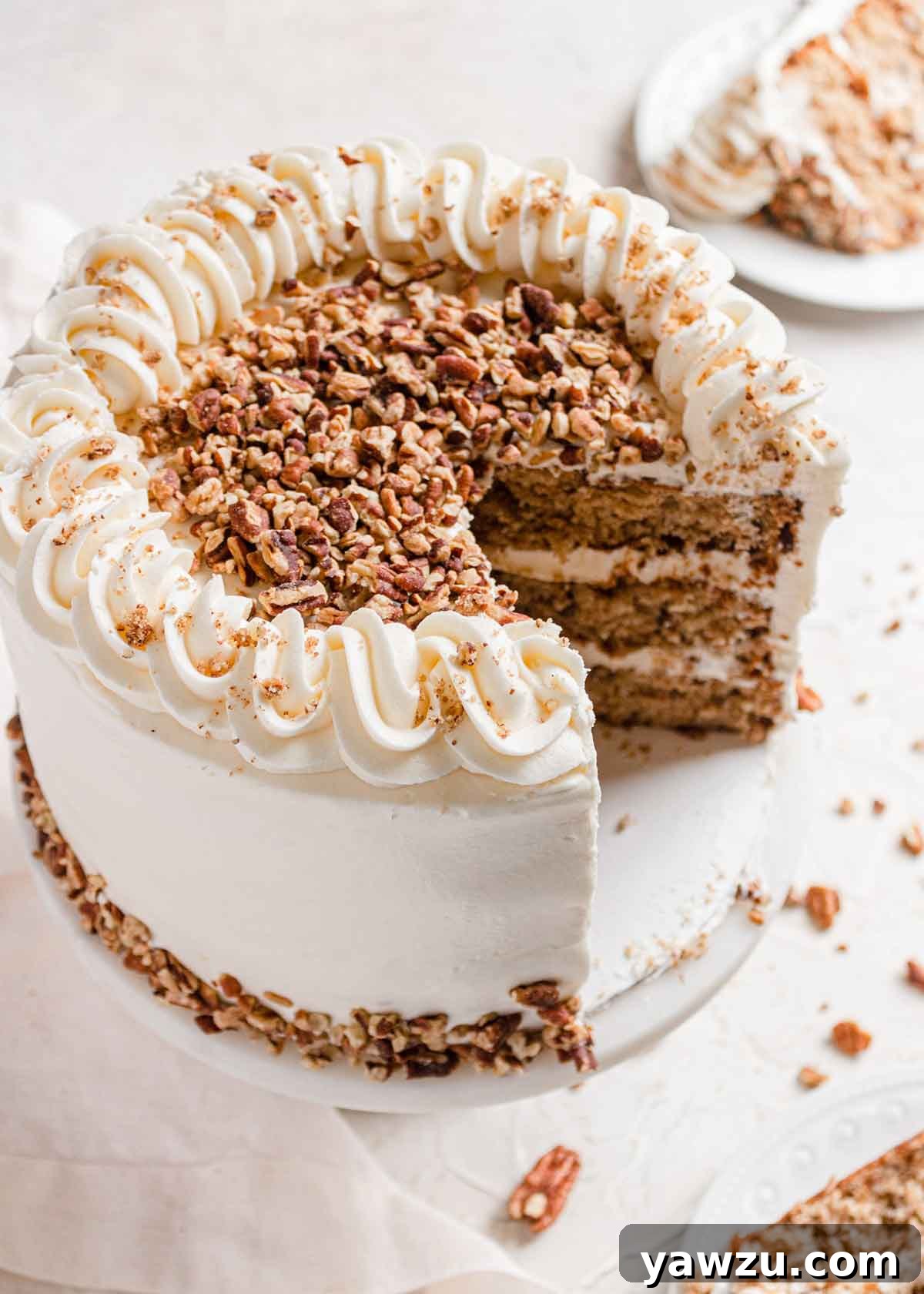 Overhead photo of hummingbird cake with two slices removed, with frosting piped around the edge and chopped pecans in the center.