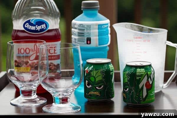 Ingredients for a layered drink: a glass with ice, cranberry juice, 7-UP, and blue Powerade. Demonstrating the components for a patriotic beverage.