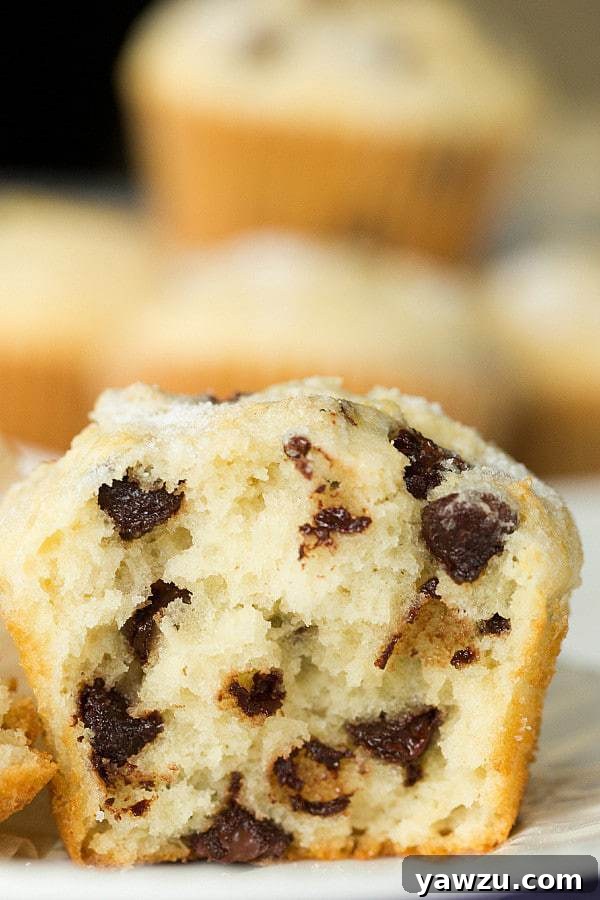 Two hands reaching for a freshly baked chocolate chip muffin on a wooden surface.